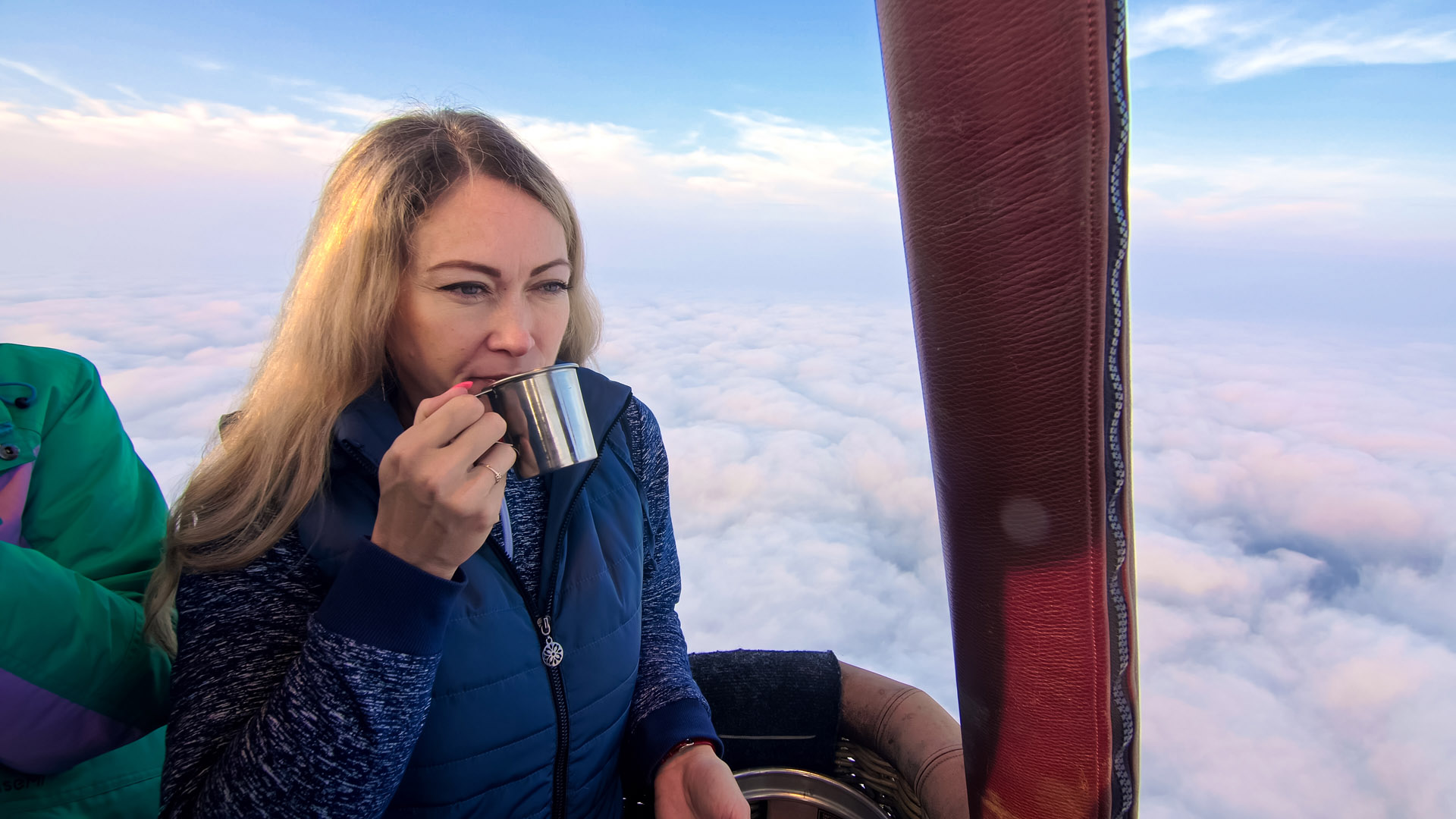 Woman eat sandwich and drinks tea and coffee in flight. Adventure on hot air balloon. Fly in morning blue sky above cloud. Girl stand in basket.